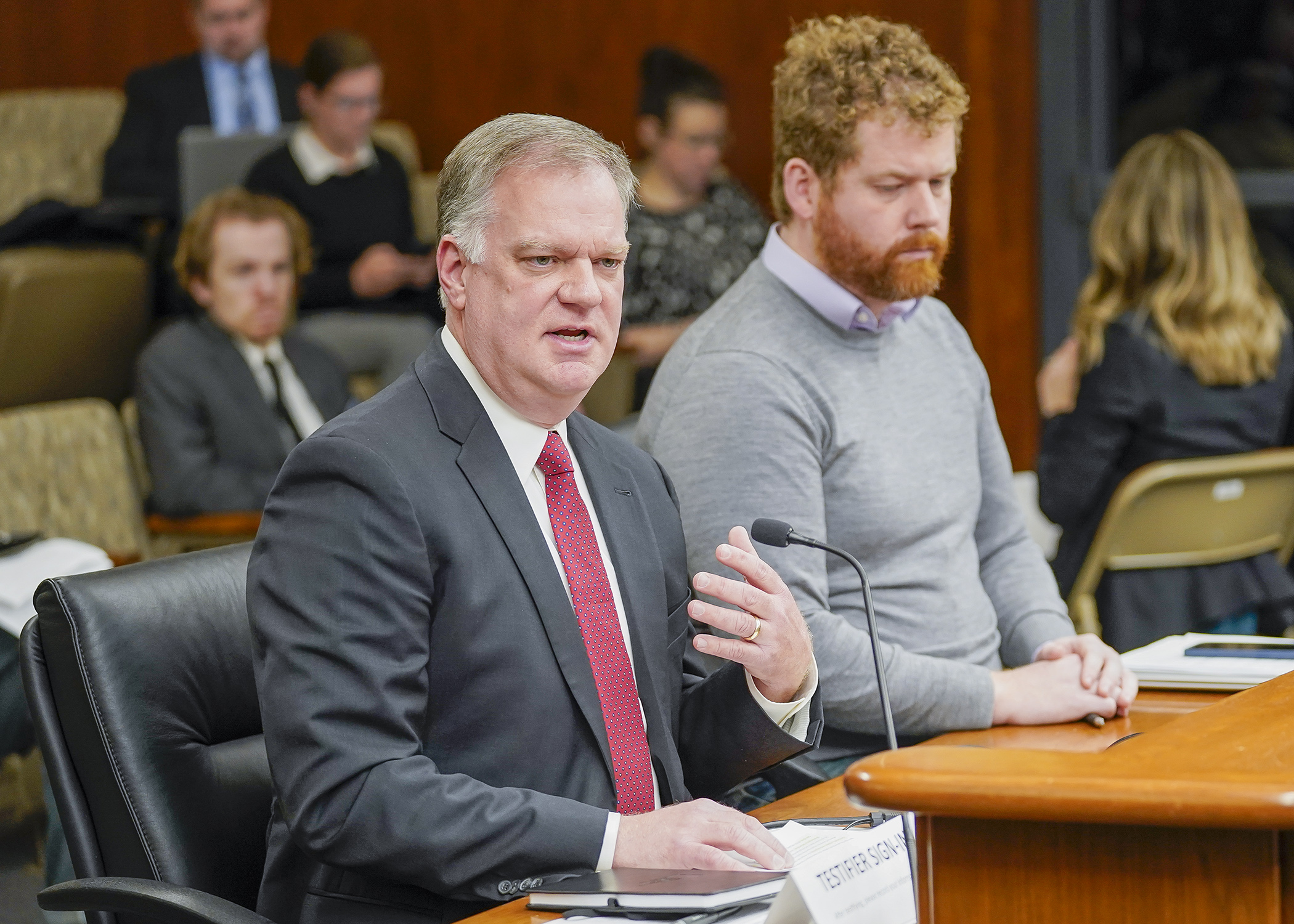Bruce Nustad, president of the Minnesota Retailers Association, testifies Jan. 9 before the House commerce committee in support of a bill sponsored by Rep. Zack Stephenson, right, that would ban price gouging during emergencies. (Photo by Andrew VonBank)